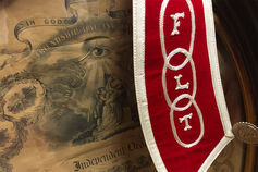 A poster for the Independent Order of Odd Fellows fraternal order and a red stole embroidered with the letters F, L, and T.